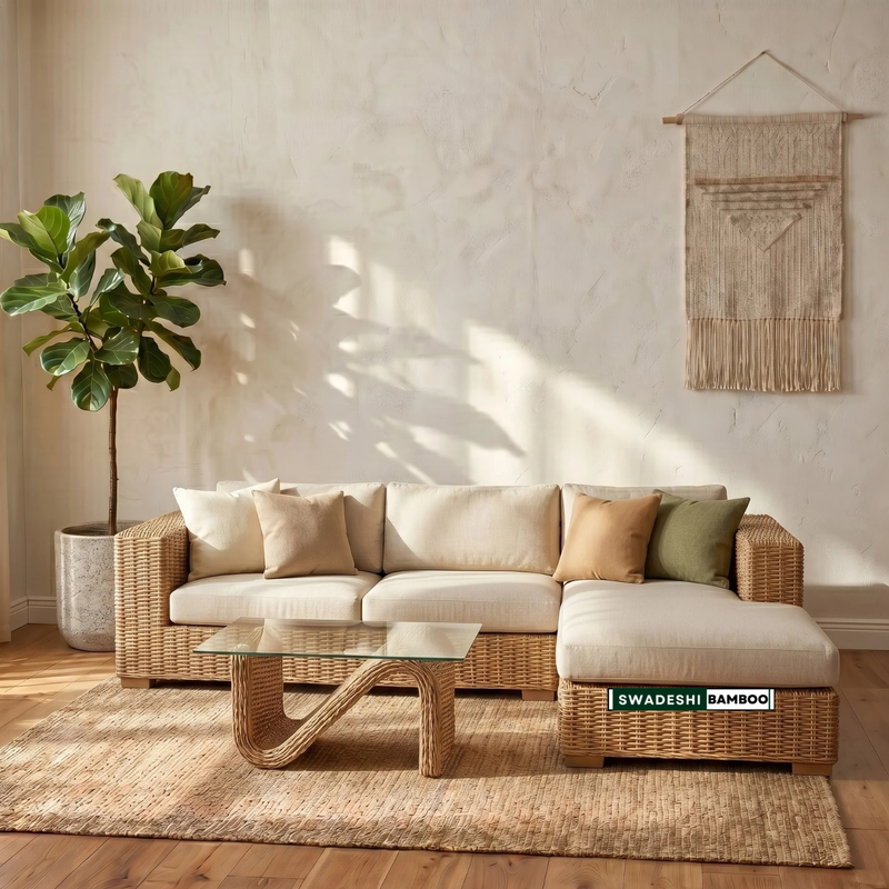 A wicker sectional sofa with cream cushions and accent pillows in a styled living room. A glass-top coffee table sits on a woven rug, with a potted fiddle-leaf fig and a wall hanging visible.