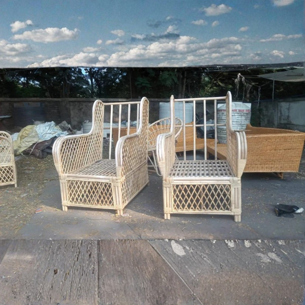Two cream-colored woven rattan armchairs with high backrests and diamond-patterned legs, displayed outdoors on a concrete surface with other furniture in the background.