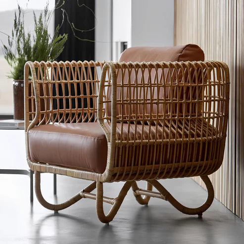 A handwoven bamboo chair with a brown cushion, featuring a curved frame and resting on a hardwood floor.